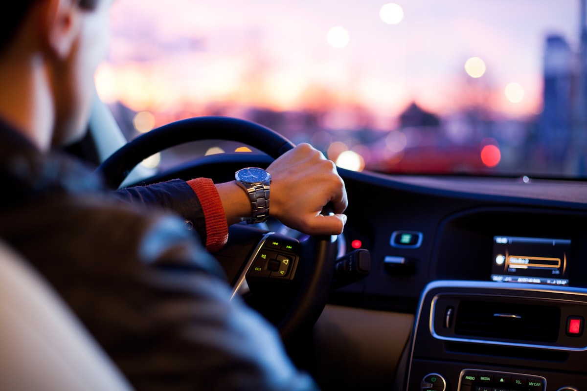 Driver's hand on the steering wheel at sunset with city lights in the distance